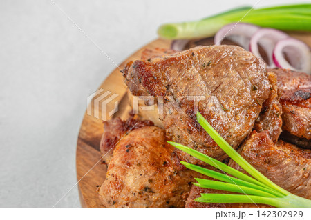 Grilled meat pieces arranged on a wooden platter with green onions and red onion slices, showcasing a delicious and appetizing presentation of cooked food Grilled meat pieces arranged on a wooden platter with green onions and red onion slices, showcasing a delicious and appetizing presentation of cooked food 142302929