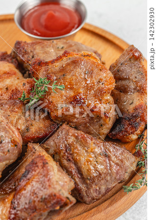 Grilled meat slices arranged on a wooden plate with a small bowl of ketchup and fresh thyme garnish, showcasing a delicious culinary presentation 142302930