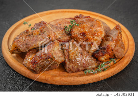 Grilled pieces of beef steak garnished with fresh thyme served on a round wooden plate against a dark textured background Grilled pieces of beef steak garnished with fresh thyme served on a round wooden plate against a dark textured background 142302931