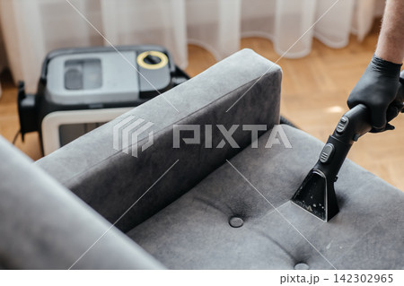 Professional upholstery cleaning with extraction vacuum cleaner on gray armchair at home Professional upholstery cleaning with extraction vacuum cleaner on gray armchair at home 142302965