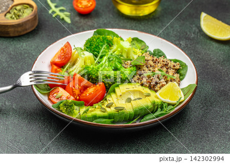 Fresh vegetable salad with avocado, broccoli, tomatoes, quinoa, and lime served in a white bowl on a dark textured surface with olive oil in the background Fresh vegetable salad with avocado, broccoli, tomatoes, quinoa, and lime served in a white bowl on a dark textured surface with olive oil in the background 142302994