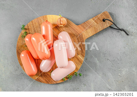 Raw sausages on wooden cutting board over gray background Raw sausages on wooden cutting board over gray background 142303201