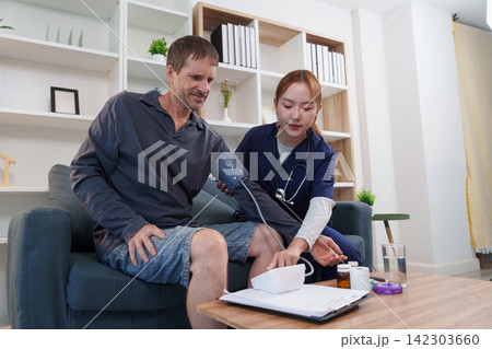 Asian home care nurse measuring blood pressure of male patient on couch Asian home care nurse measuring blood pressure of male patient on couch 142303660