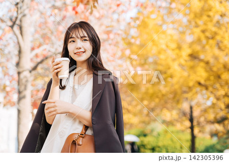 銀杏がきれいな街をコーヒーを持って歩く女性 銀杏がきれいな街をコーヒーを持って歩く女性 142305396