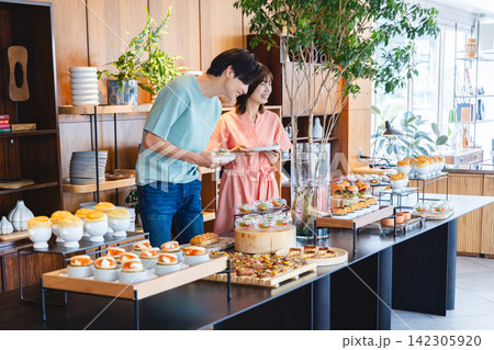 ビュッフェスタイルのランチで料理を選ぶ若いカップル ビュッフェスタイルのランチで料理を選ぶ若いカップル 142305920