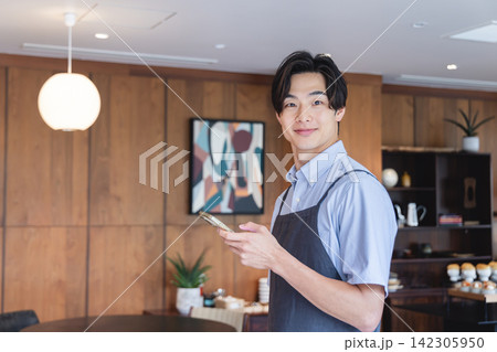 スマートフォンでオーダーをとるカフェの男性スタッフ 142305950