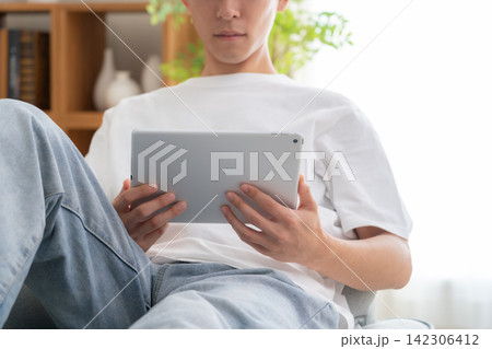 家でタブレットを見る若い男性 家でタブレットを見る若い男性 142306412