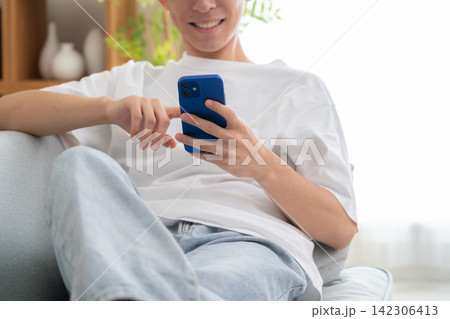 家でスマホを見る若い男性 142306413