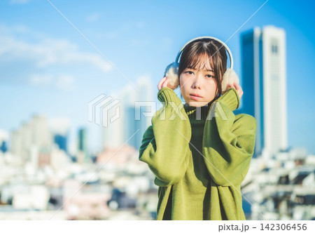 耳当てをした笑顔の女性と都会のビル群 耳当てをした笑顔の女性と都会のビル群 142306456
