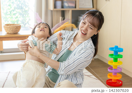 子供の着替えがうまくいかなくてイライラしている母親 子供の着替えがうまくいかなくてイライラしている母親 142307020