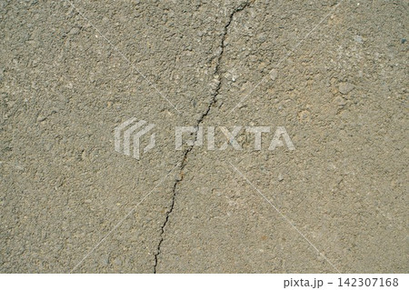 A top-down close-up shot of an uneven grey asphalt surface featuring a continuous vertical narrow crack A top-down close-up shot of an uneven grey asphalt surface featuring a continuous vertical narrow crack 142307168