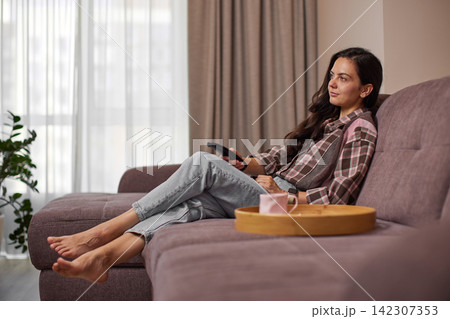 Woman relaxing at home watching tv on sofa Woman relaxing at home watching tv on sofa 142307353