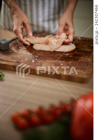 Hands preparing raw chicken breast on wooden board Hands preparing raw chicken breast on wooden board 142307466
