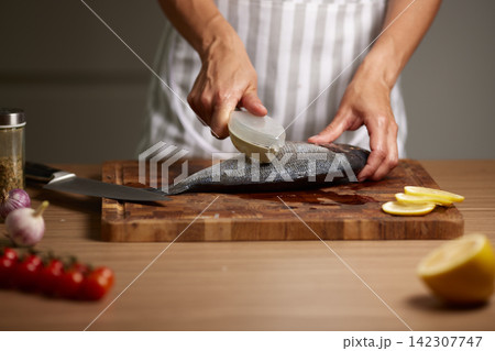 Person descaling fish on cutting board in kitchen Person descaling fish on cutting board in kitchen 142307747