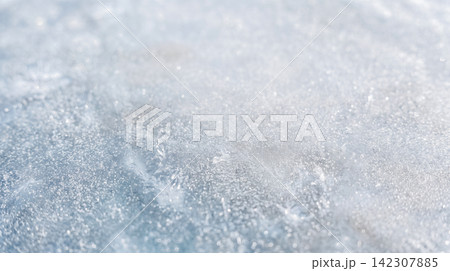 Close macro view showing solid frozen water surface featuring deep cracks across thick light blue ice layer under bright cold winter weather 142307885