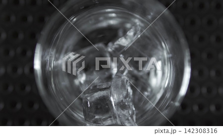 Clear glass with ice cubes filling up on dark bar surface, showing refreshing cold drink concepts and hospitality Clear glass with ice cubes filling up on dark bar surface, showing refreshing cold drink concepts and hospitality 142308316
