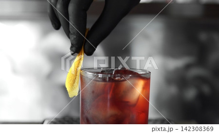 Bartender garnishing negroni cocktail with lemon peel, preparing alcoholic drink at bar for clients Bartender garnishing negroni cocktail with lemon peel, preparing alcoholic drink at bar for clients 142308369