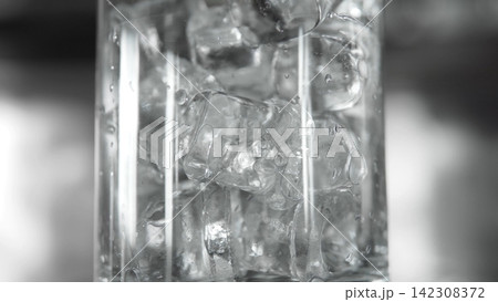 Clear ice cubes filling a transparent glass, creating a refreshing cold drink with water droplets and condensation 142308372