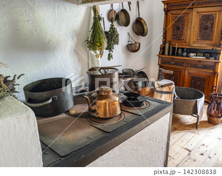 Vintage Rural Kitchen Interior With Antique Copper Kettle, Pots and Hanging Herbs on Wood Stove 142308838
