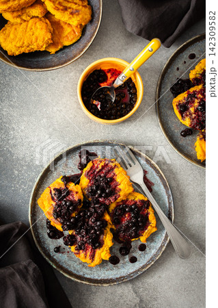 Millet pancakes are arranged on a plate and topped with currant sauce. The scene displays a simple breakfast setting at home in the morning Millet pancakes are arranged on a plate and topped with currant sauce. The scene displays a simple breakfast setting at home in the morning 142309582