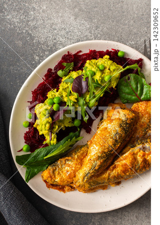 Baked small sea fish is served alongside boiled beets, hummus, green peas, and herbs. This dish is suitable for breakfast and offers a healthy option 142309652