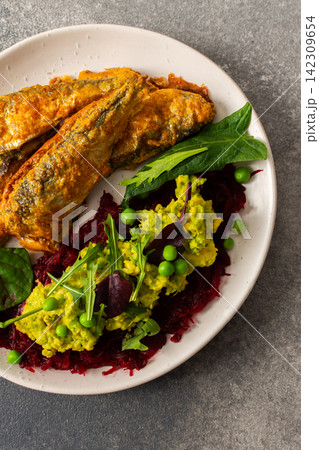 Baked small sea fish is served alongside boiled beets, hummus, green peas, and herbs. This dish is suitable for breakfast and offers a healthy option 142309654