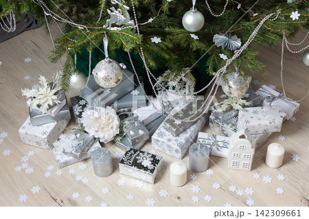 Steel-colored gift boxes paired with glowing candles and delicate decorations under a lush Christmas tree, creating an elegant and festive holiday atmosphere Steel-colored gift boxes paired with glowing candles and delicate decorations under a lush Christmas tree, creating an elegant and festive holiday atmosphere 142309661