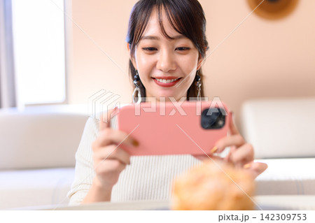 スマートフォンでスイーツを撮影し笑顔を見せる女性 142309753
