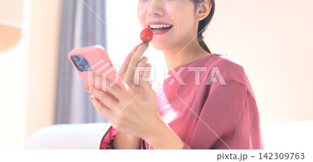スマホを見ながらミニトマトを食べる女性 スマホを見ながらミニトマトを食べる女性 142309763