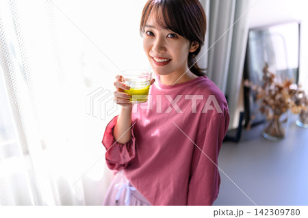 朝の光の中でグリーンスムージーを飲む笑顔の若い女性 朝の光の中でグリーンスムージーを飲む笑顔の若い女性 142309780