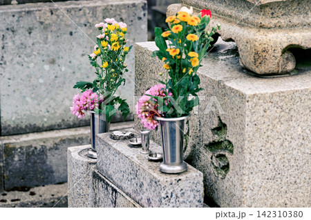 墓石に供えられた色鮮やかな花と金属製の花立て 墓石に供えられた色鮮やかな花と金属製の花立て 142310380