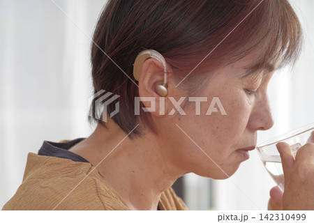 耳かけ型補聴器を使用するシニア女性 耳かけ型補聴器を使用するシニア女性 142310499