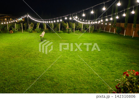 A serene, nighttime grassy backyard illuminated by bright white electric lights A serene, nighttime grassy backyard illuminated by bright white electric lights 142310806