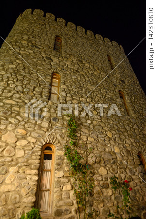 A low-angle nighttime photograph capturing an ancient stone tower with textured stonework and arched windows 142310810