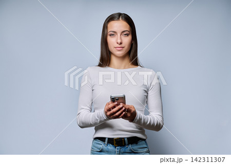 Young woman holding smartphone looking at camera studio portrait 142311307