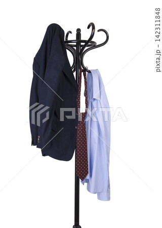 A dark blue blazer, a patterned tie, and a light blue dress shirt hang on a black coat rack. A dark blue blazer, a patterned tie, and a light blue dress shirt hang on a black coat rack. 142311848