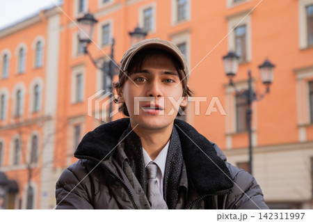 Young student man wearing casual clothes and cap standing in city street. Portrait of male learner in urban environment. Education, youth lifestyle, study and academic development concept. Young student man wearing casual clothes and cap standing in city street. Portrait of male learner in urban environment. Education, youth lifestyle, study and academic development concept. 142311997