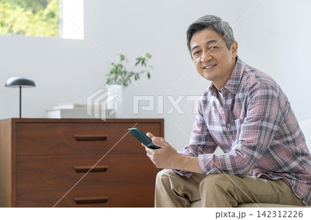 スマートフォンを持ったカメラ目線で笑顔の60代の男性 スマートフォンを持ったカメラ目線で笑顔の60代の男性 142312226