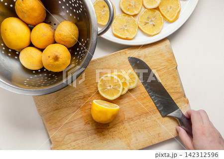 Hand Cutting a Fresh Garden Lemon on a Wooden Cutting Board with Slices on a White Plate Hand Cutting a Fresh Garden Lemon on a Wooden Cutting Board with Slices on a White Plate 142312596