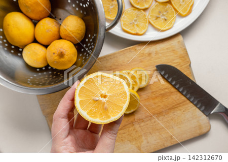 Hand Cutting a Fresh Garden Lemon on a Wooden Cutting Board with Slices on a White Plate Hand Cutting a Fresh Garden Lemon on a Wooden Cutting Board with Slices on a White Plate 142312670