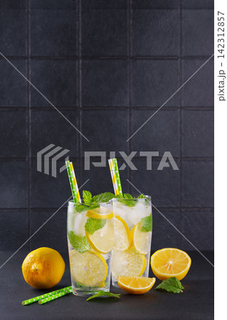 Fresh homemade lemonade with lemon slices, mint and ice in glasses on black kitchen tile background Fresh homemade lemonade with lemon slices, mint and ice in glasses on black kitchen tile background 142312857