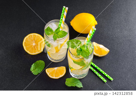 Cold homemade lemonade with fresh lemon, mint and ice in glasses on black textured stone background 142312858