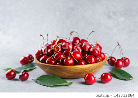 Fresh ripe sweet cherry in wooden bowl with green leaves on light background, healthy organic fruit 142312864