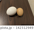 Comparison of natural farm fresh brown egg and industrially produced perfect white egg on dark wood contrast 142312949