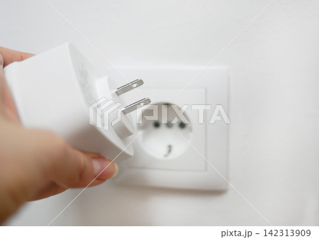 Universal travel adapter in a hand close up against the backdrop of a socket. Electric plug adapter, international plug gadget for travel. Universal travel adapter in a hand close up against the backdrop of a socket. Electric plug adapter, international plug gadget for travel. 142313909