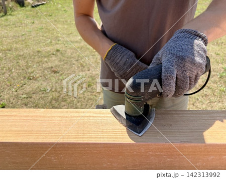 a worker sanding a light wooden board with a detail power sander during renovation. A home renovation, carpentry, or DIY woodworking project. 142313992