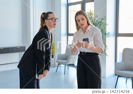 Two businesswomen looking at smartphone in modern office Two businesswomen looking at smartphone in modern office 142314256
