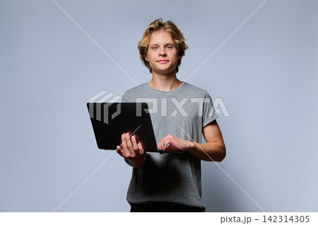 Portrait of teenage student holding open laptop and typing 142314305