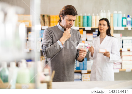 Man chooses packages with pills against the background of pharmacist Man chooses packages with pills against the background of pharmacist 142314414