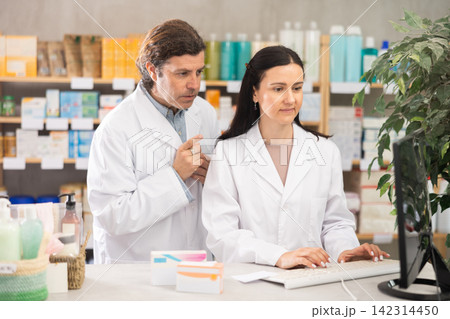 man and a woman pharmacist working at a computer in a pharmacy man and a woman pharmacist working at a computer in a pharmacy 142314450